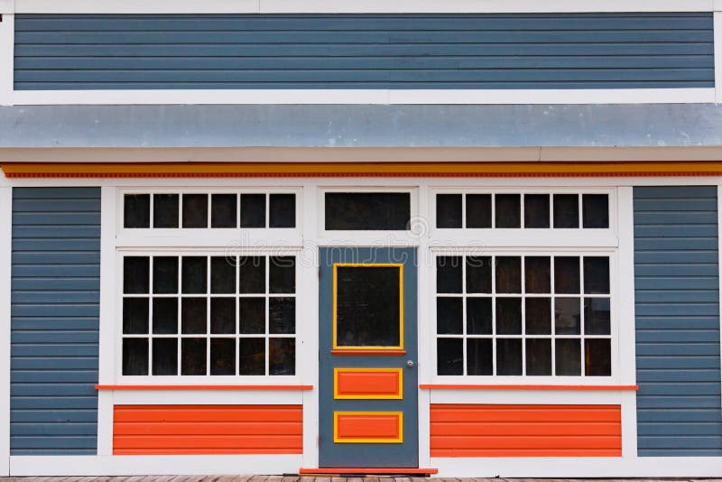 Symmetrical view of the front door and entrance to a quaint colorful wooden house with large cottage pane windows on either side. Symmetrical view of the front door and entrance to a quaint colorful wooden house with large cottage pane windows on either side