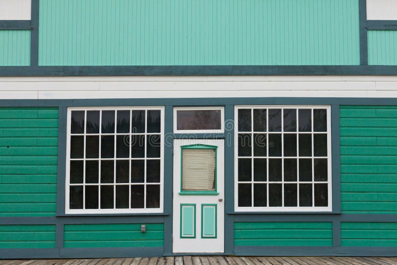 Symmetrical view of the front door and entrance to a quaint green wooden house with large cottage pane windows on either side. Symmetrical view of the front door and entrance to a quaint green wooden house with large cottage pane windows on either side