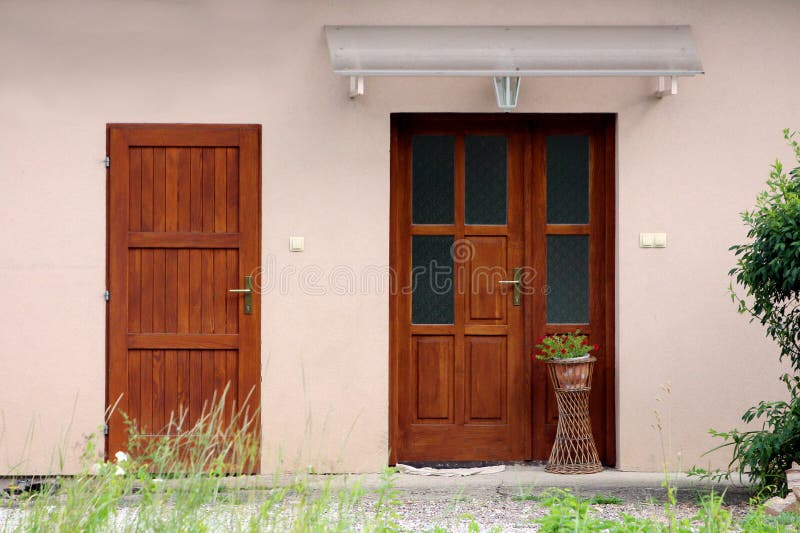 Small suburban family house new rustic looking wooden entrance doors with flower pot and red flowers covered with transparent