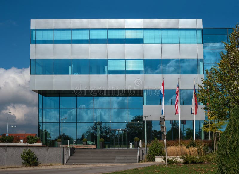 Small suburban office building. Glass and concrete. In front of the entrance are flagpoles. Glasses of blue