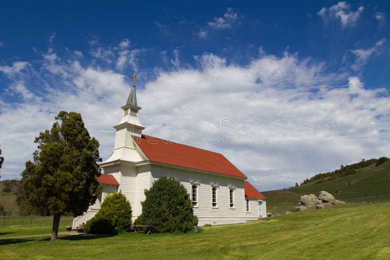 Side angle of a little white church with a red roof in Northern California with patchy blue skies