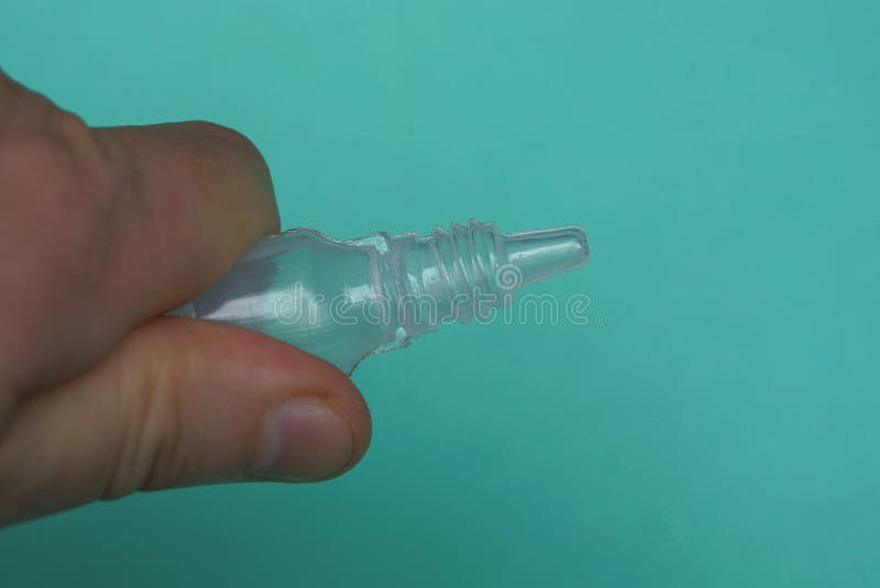 Small plastic bottle with drops in fingers of hand on a green background