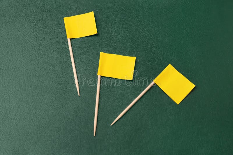 Small yellow paper flags on green background, flat lay stock images