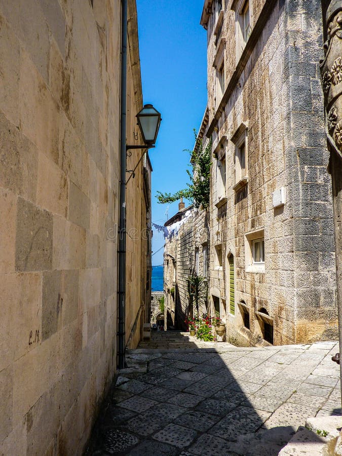 Smalle die straat door huizen met stappen - neer en een mening van het overzees in Korcula, Kroatië wordt gevoerd stock foto's Smalle die straat door huizen met stappen - neer en een mening van het overzees in Korcula, Kroatië wordt gevoerd stock foto's