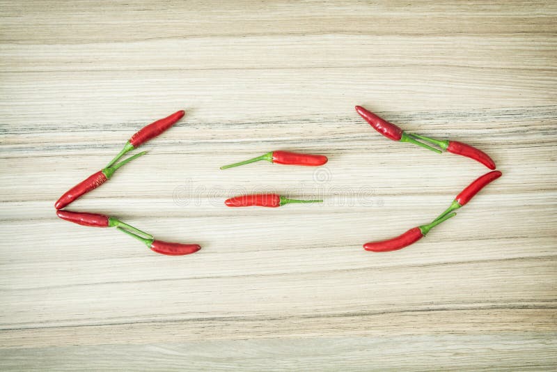 Smaller-than, greater-than and equal sign of chilli peppers on the wooden background.
