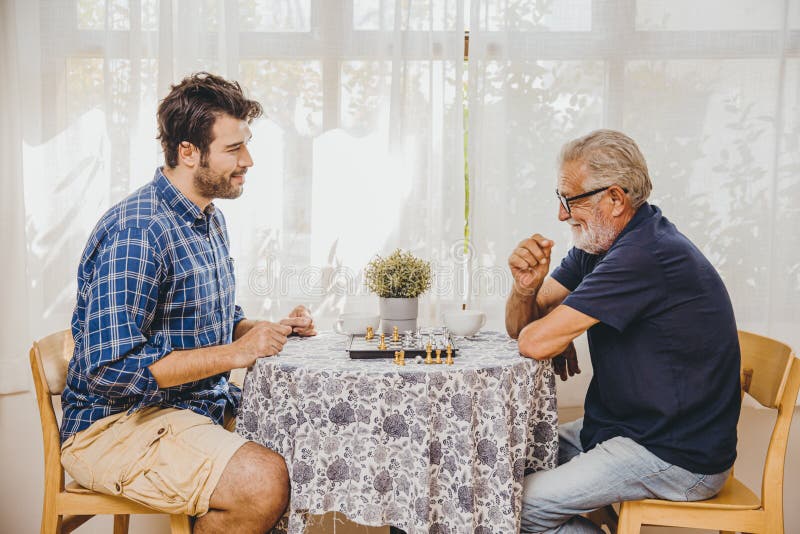 Smart elder playing chess board game at home care with younger man for stay brain healthy. Smart elder playing chess board game at home care with younger men for stock image