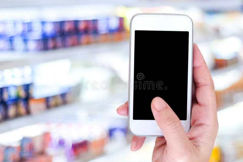 Hand holding smart phone over blur supermarket background, retail business , shopping online and technology concept. Hand holding smart phone over blur supermarket background, retail business , shopping online and technology concept