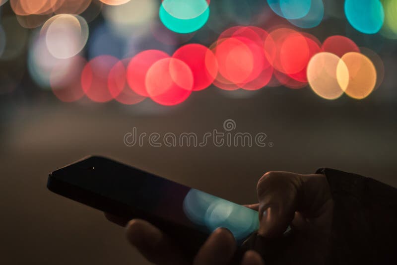 Smart phone in male hands in front of blurred city lights