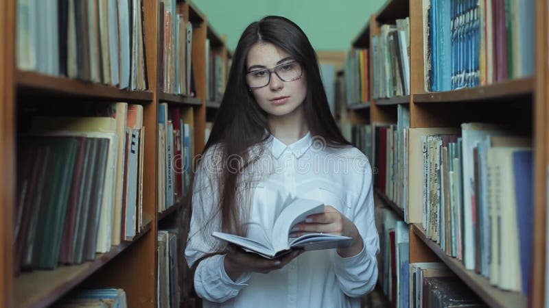 Smart se och härlig ung flicka i den vita skjortan och exponeringsglas i collageskolaarkivet som väljer boken att läsa arkivfilmer
