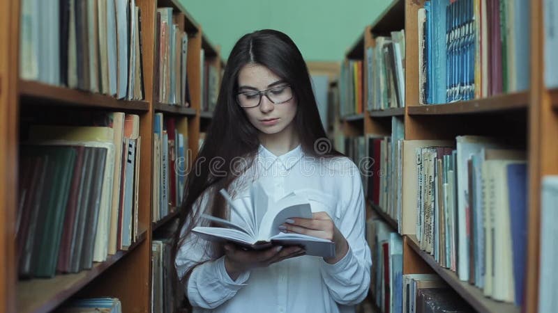 Smart se och härlig ung flicka i den vita skjortan och exponeringsglas i collageskolaarkivet som väljer boken att läsa arkivfilmer