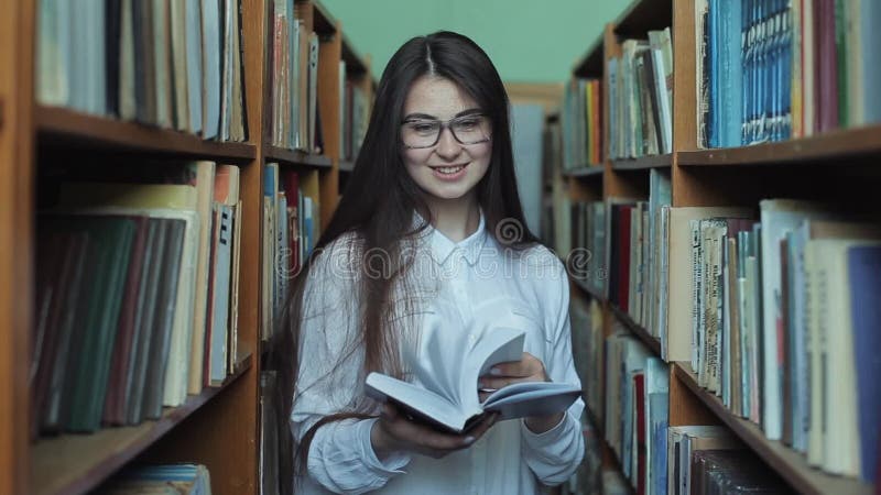 Smart se och härlig ung flicka i den vita skjortan och exponeringsglas i collageskolaarkivet som väljer boken att läsa arkivfilmer