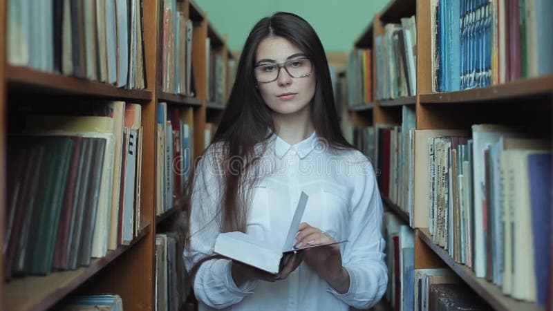 Smart se och härlig ung flicka i den vita skjortan och exponeringsglas i collageskolaarkivet som väljer boken att läsa stock video