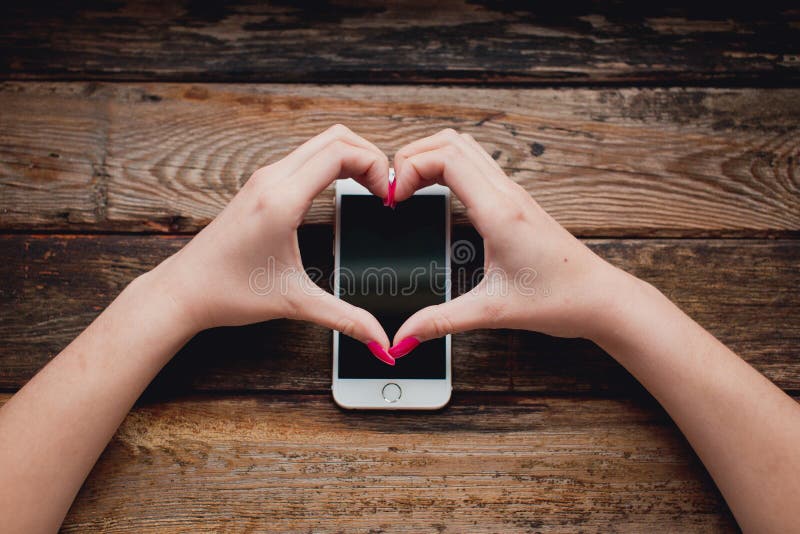 Smartphone blanc dans des mains femelles sur un fond en bois image stock Smartphone blanc dans des mains femelles sur un fond en bois image stock