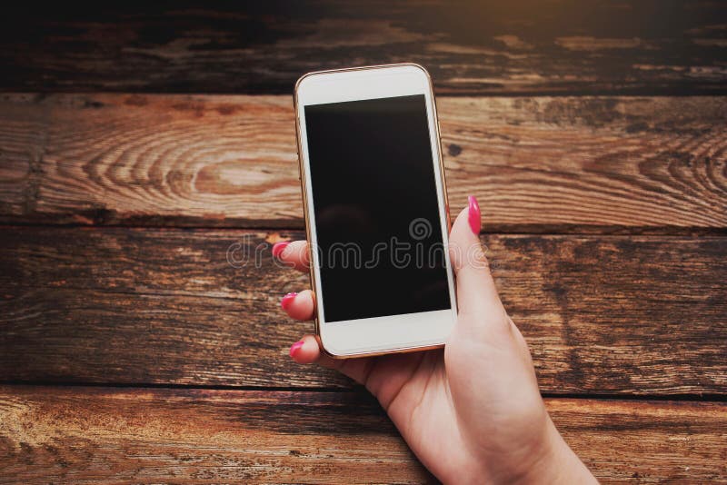 Smartphone branco nas mãos fêmeas em um fundo de madeira foto de stock Smartphone branco nas mãos fêmeas em um fundo de madeira foto de stock