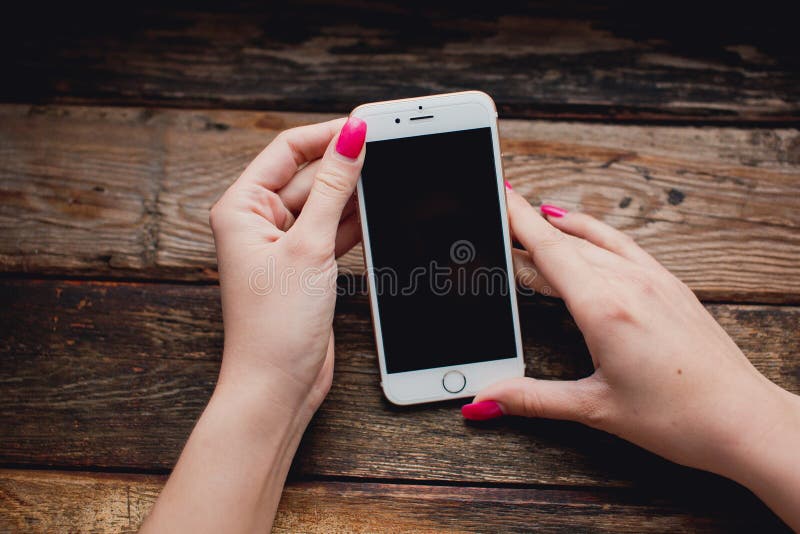 Smartphone branco nas mãos fêmeas em um fundo de madeira imagem de stock Smartphone branco nas mãos fêmeas em um fundo de madeira imagem de stock