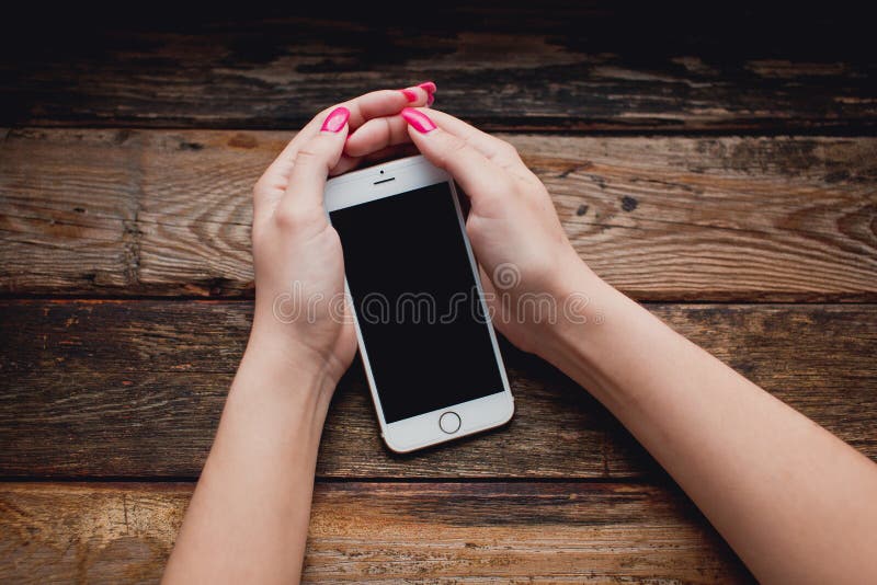 Smartphone branco nas mãos fêmeas em um fundo de madeira fotografia de stock Smartphone branco nas mãos fêmeas em um fundo de madeira fotografia de stock