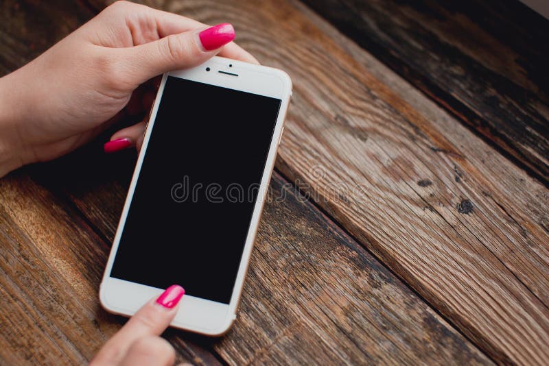 Smartphone branco nas mãos fêmeas em um fundo de madeira fotos de stock Smartphone branco nas mãos fêmeas em um fundo de madeira fotos de stock