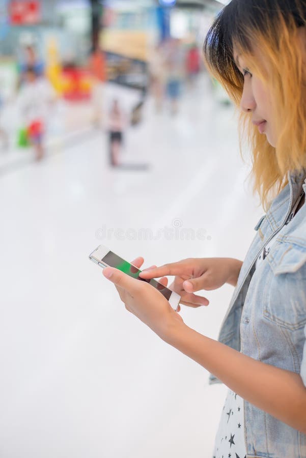 Smartphone di battitura a macchina della tenuta della mano della giovane donna a chiacchierata alla m. di compera fotografia stock libera da diritti Smartphone di battitura a macchina della tenuta della mano della giovane donna a chiacchierata alla m. di compera fotografia stock libera da diritti