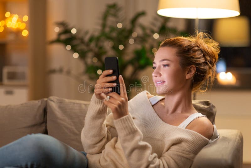 Ευτυχής νέα γυναίκα με το smartphone στο σπίτι. Technology and people concept - happy young woman with smartphone at home in evening