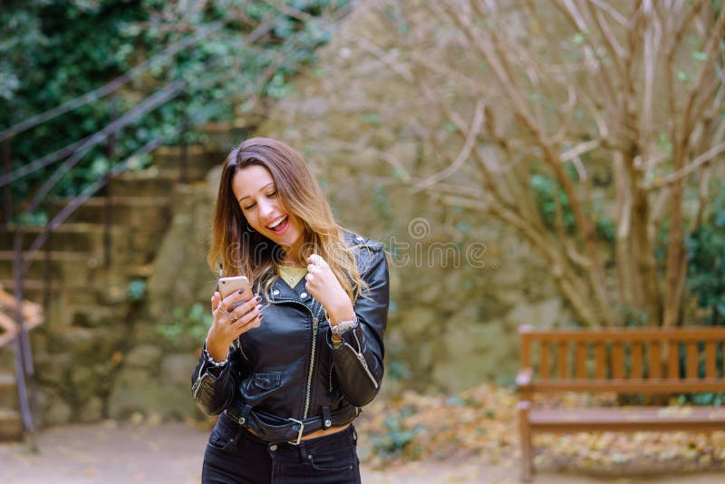 Smartphone entusiasmado da consultação da mulher no parque imagem de stock royalty free