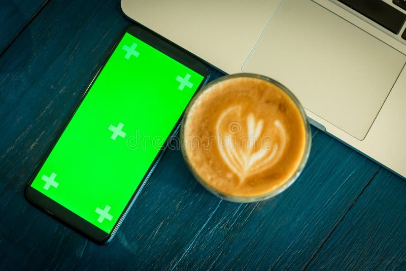 Smartphone med den gröna skärmen nära kaffe och bärbara datorn royaltyfri bild Smartphone med den gröna skärmen nära kaffe och bärbara datorn royaltyfri bild