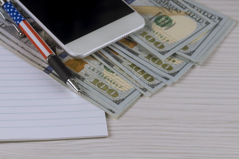 Smartphone, a notebook and pen on hundred dollar bills