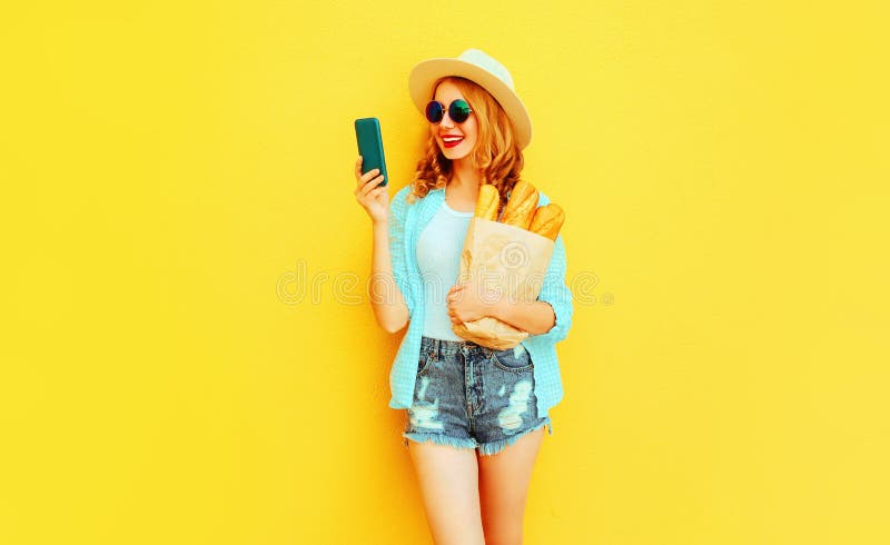 Smartphone sonriente feliz de la tenencia de la mujer del retrato, bolsa de papel con el baguette largo del pan blanco, sombrero imágenes de archivo libres de regalías Smartphone sonriente feliz de la tenencia de la mujer del retrato, bolsa de papel con el baguette largo del pan blanco, sombrero imágenes de archivo libres de regalías