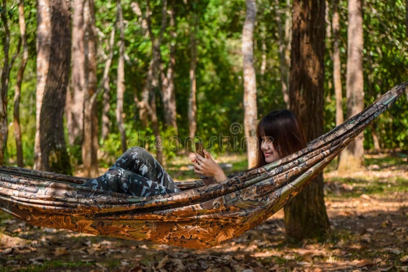 Smartphone usando femminile mentre riposando in amaca nell'attivit? di campeggio in foresta immagine stock libera da diritti Smartphone usando femminile mentre riposando in amaca nell'attivit? di campeggio in foresta immagine stock libera da diritti