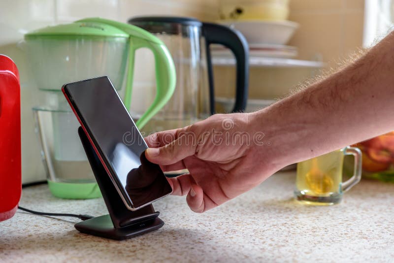 Smartphone wireless charging on charging stand on kitchen tabletop. male hand placing phone to charging