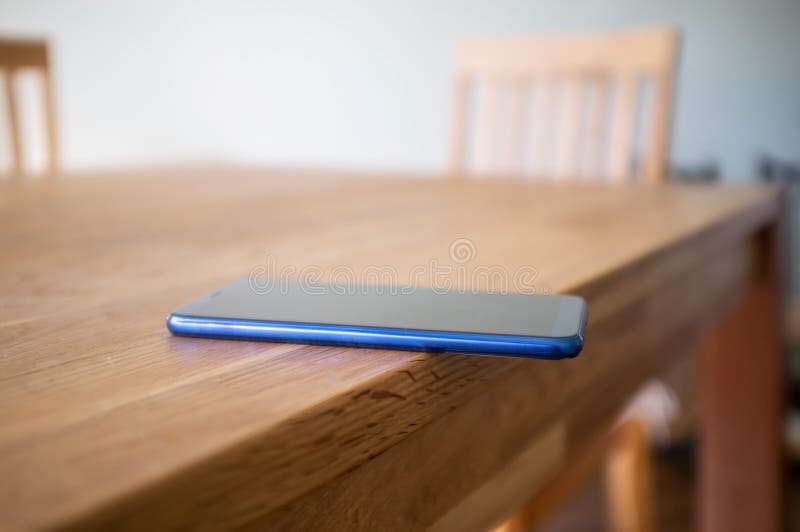 Smartphone är skoningslöst placerad på kanten av ett träbord och kan falla. Begreppet vårdslös attityd till saker och ting. arkivbild