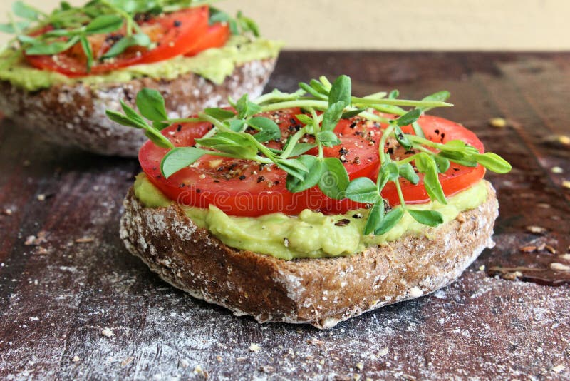 Smashed avocado and tomato toast with herbs on wooden table