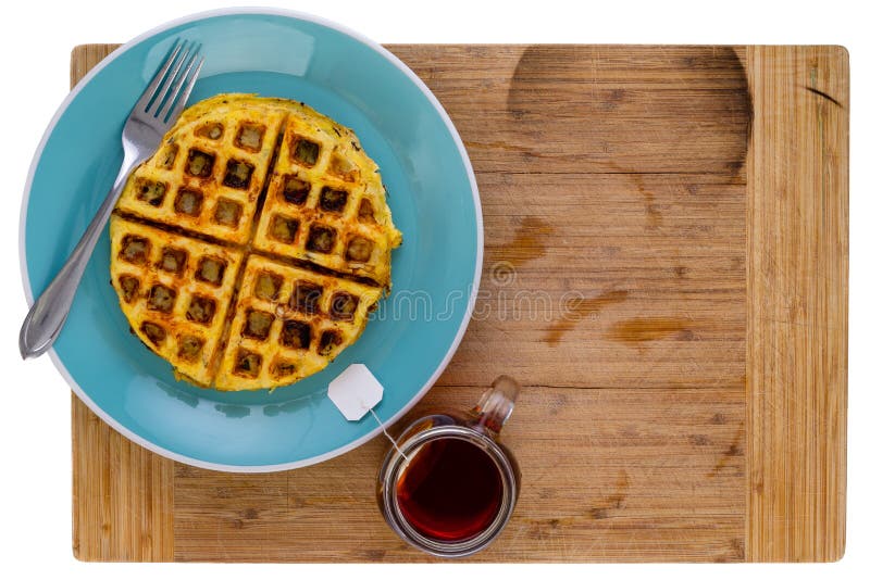 Golden crispy fried hash brown with honey comb waffle pattern on a blue plate with a teabag steeping in a mug of hot water alongside in an overhead view on a wooden board with copy space. Golden crispy fried hash brown with honey comb waffle pattern on a blue plate with a teabag steeping in a mug of hot water alongside in an overhead view on a wooden board with copy space.