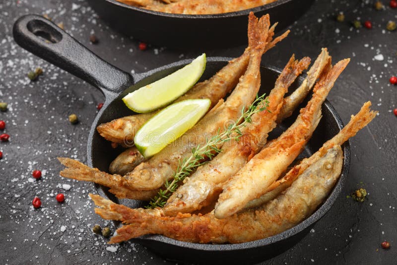 Fried smelt in a frying pan on the table with spices, lime and thyme. Small crispy fish. Selective focus. Fried smelt in a frying pan on the table with spices, lime and thyme. Small crispy fish. Selective focus