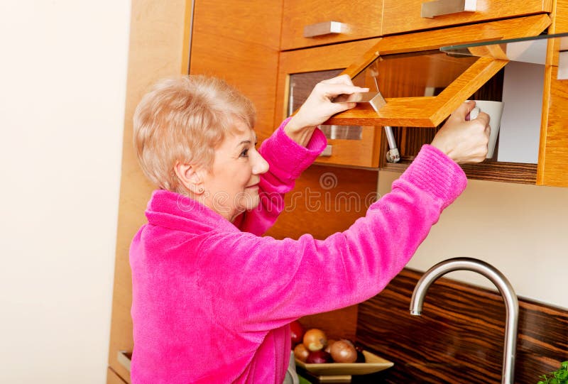 Smile senior woman taking mug from a kitchen cabinet royalty free stock photography Smile senior woman taking mug from a kitchen cabinet royalty free stock photography