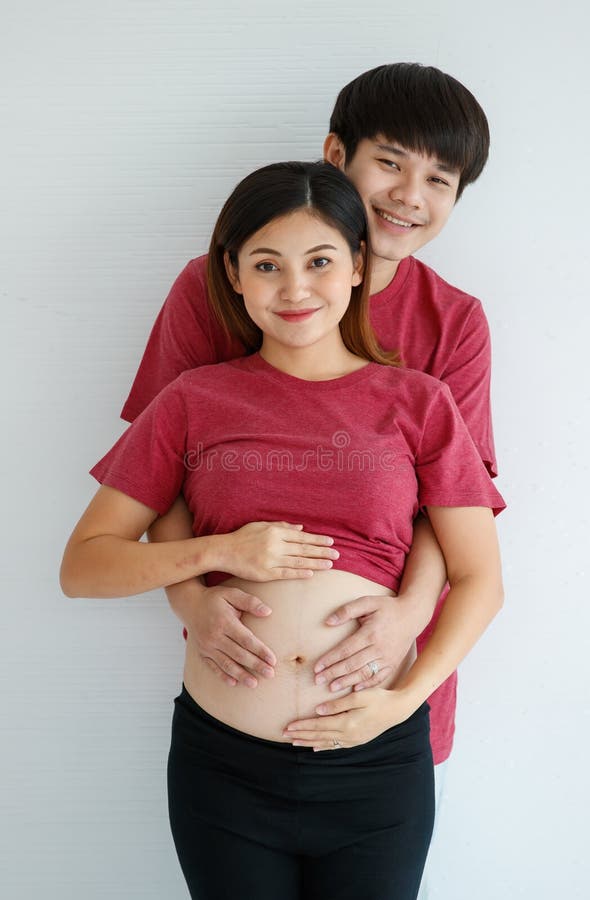 Asian pregnant woman in black undershirt sitting on white bed and
