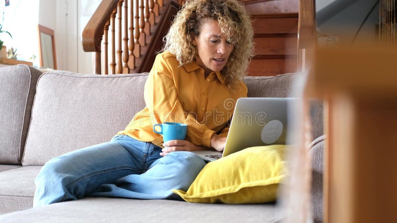 Smiling adult young woman sit relax on couch using modern laptop browsing unlimited wireless internet, happy young people