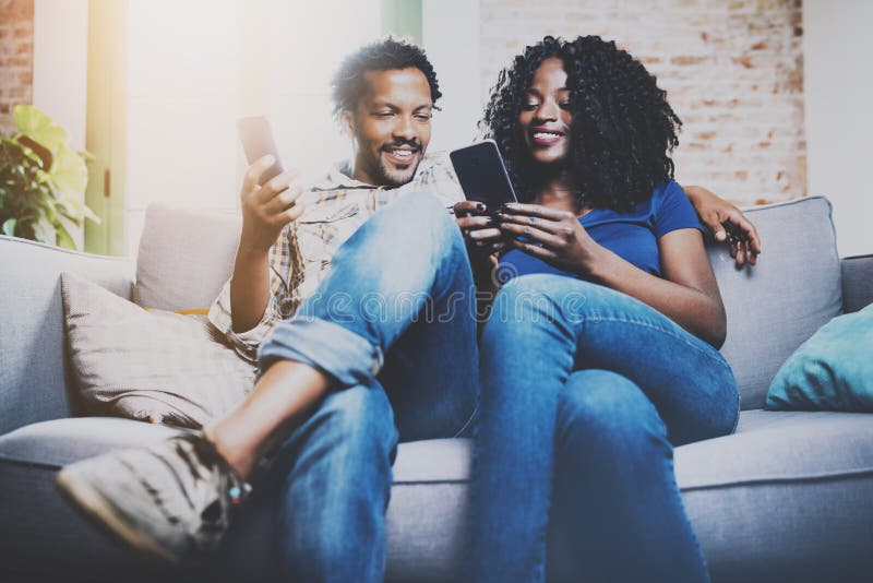 Smiling african american couple relaxing together on the sofa.Young black man and his girlfriend using smartphones while royalty free stock images Smiling african american couple relaxing together on the sofa.Young black man and his girlfriend using smartphones while royalty free stock images