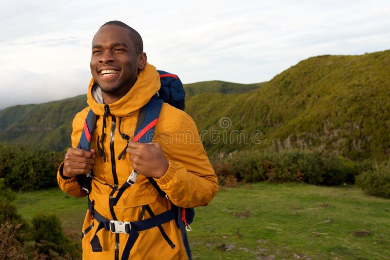 Smiling african american hiker walking with backpack in nature stock photo