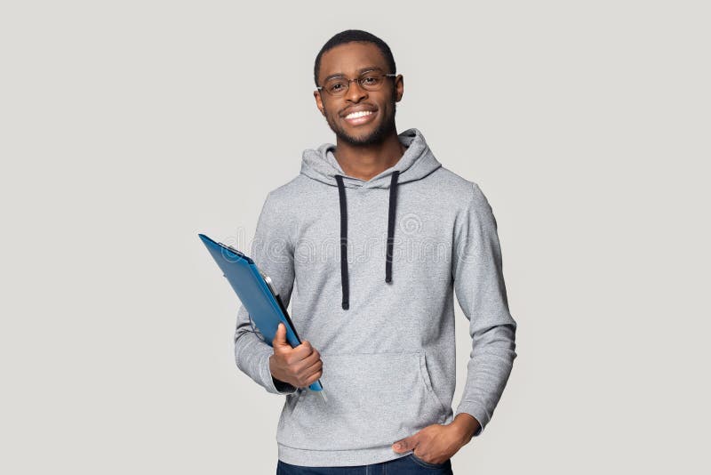 Smiling african American man in glasses isolated on grey studio background look at camera keep documents in hand, happy black male student or employee stand holding binder case and gadget. Smiling african American man in glasses isolated on grey studio background look at camera keep documents in hand, happy black male student or employee stand holding binder case and gadget