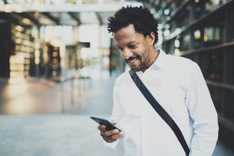 Smiling African American man holding mobile phone in hands and checking email.Blurred background.