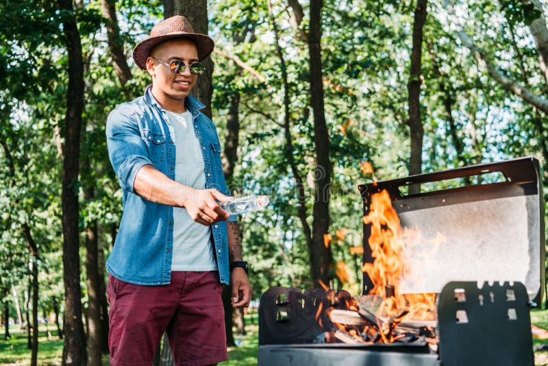 smiling african american man in sunglasses and hat setting fire on grill