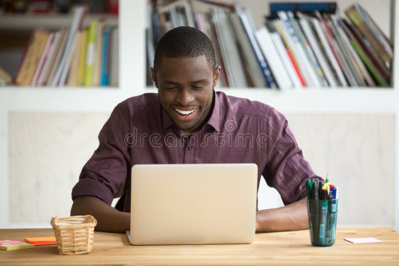 Smiling african-american man using laptop sitting at home office