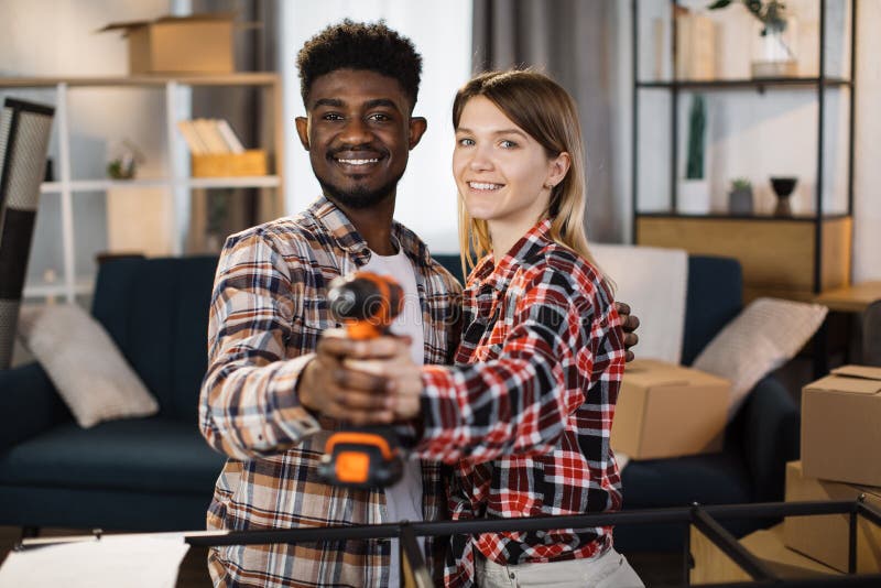 Diverse couple posing at new flat with screwdriver in hands royalty free stock photo