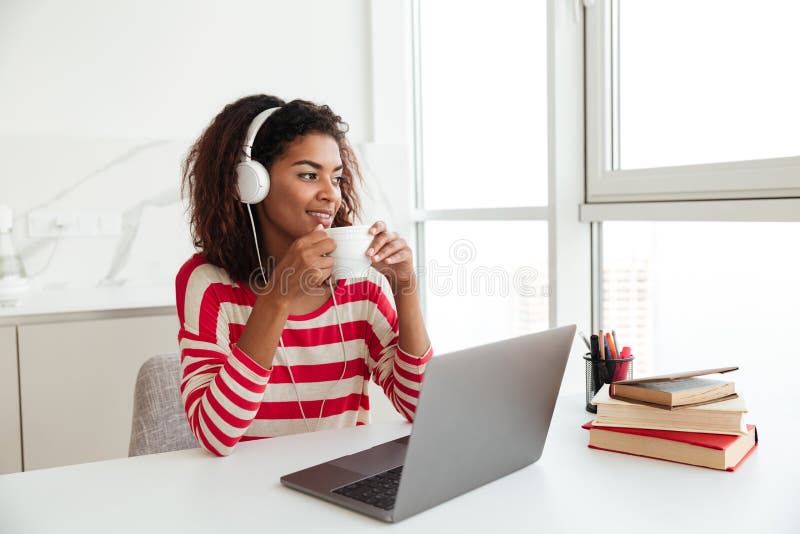 Smiling african woman sitting by the table with laptop computer