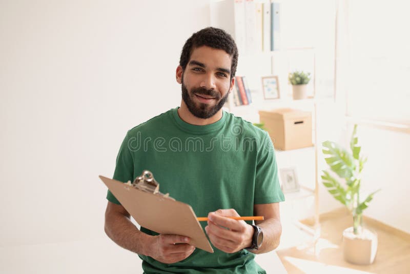 Smiling arabic man in green t-shirt work with documents and contemplating with pencil