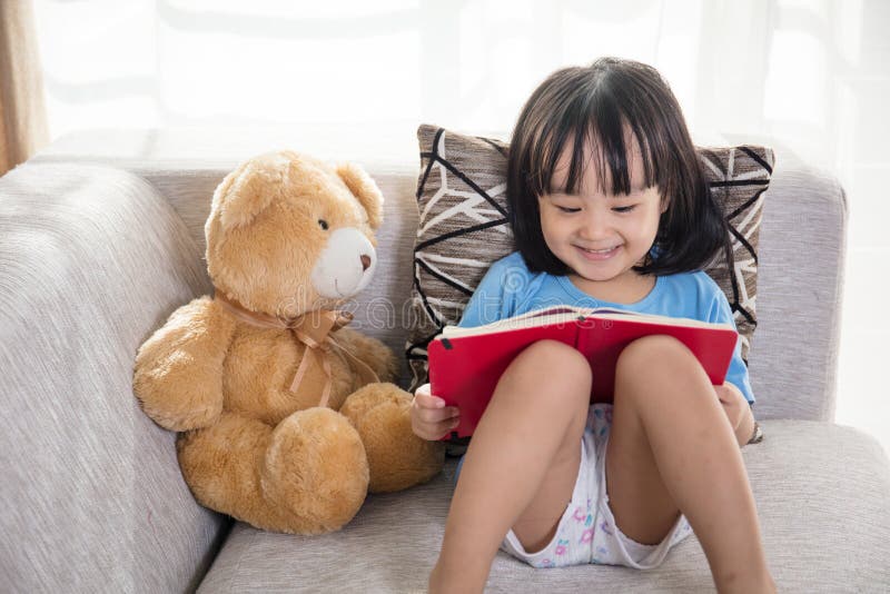 Smiling Asian Chinese little girl reading book with teddy bear