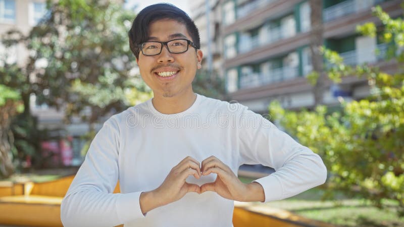 Smiling asian man making heart shape with hands in sunny park royalty free stock photo