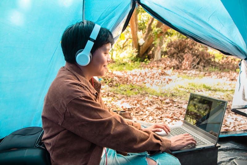Smiling Asian people wearing headphones listening podcast music online on a laptop he is sitting in the tent vacation relaxing. Smiling Asian people wearing royalty free stock image