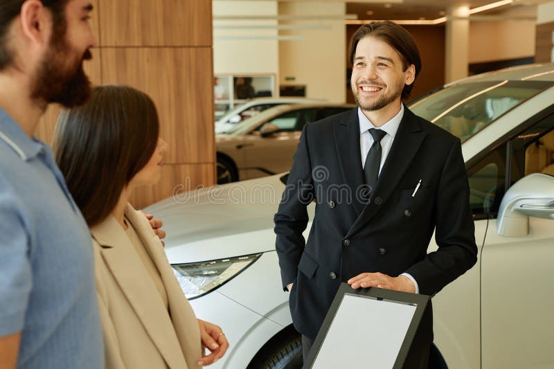 Smiling Auto Dealer Talking to Clients at Car Dealership Center stock images
