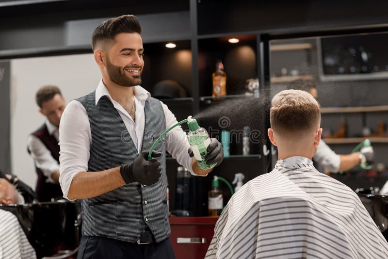 Smiling barber sprinkling water on client`s haircut using sprayer bottle. royalty free stock photo Smiling barber sprinkling water on client`s haircut using sprayer bottle. royalty free stock photo